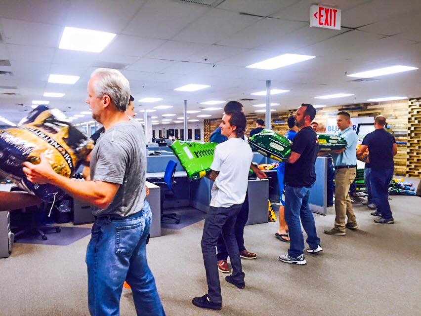 BlueGrace employees in an office setting carrying large bags of supplies, likely for a community event.