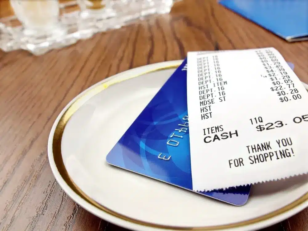 Restaurant receipt for $23.05 and a blue credit card on a white plate with "Thank you for shopping" text.