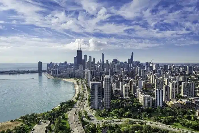 Aerial view of the Chicago skyline and Lake Michigan coastline under a blue sky with white clouds.