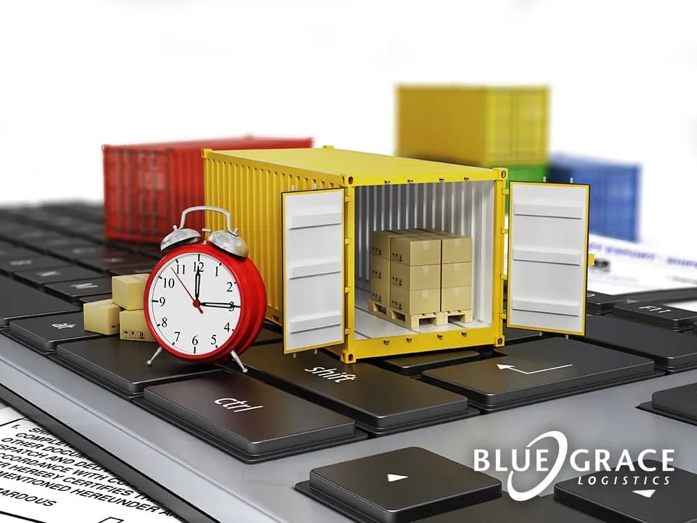Miniature shipping container on a laptop keyboard next to an alarm clock with the BlueGrace Logistics logo.