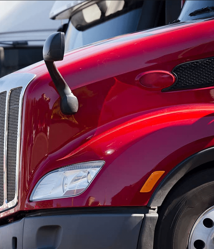 A detailed, close-up shot of the front passenger side of a polished red semi-truck, highlighting the aerodynamic hood, headlight assembly, and side-view mirror.
