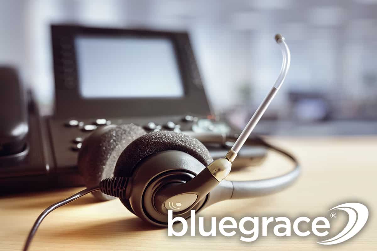 Close-up of an office headset and telephone on a desk with the BlueGrace logo.
