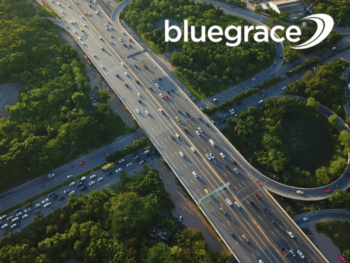 An aerial view of a multi-lane highway interchange surrounded by dense green forest, featuring the BlueGrace logo in the top right corner.