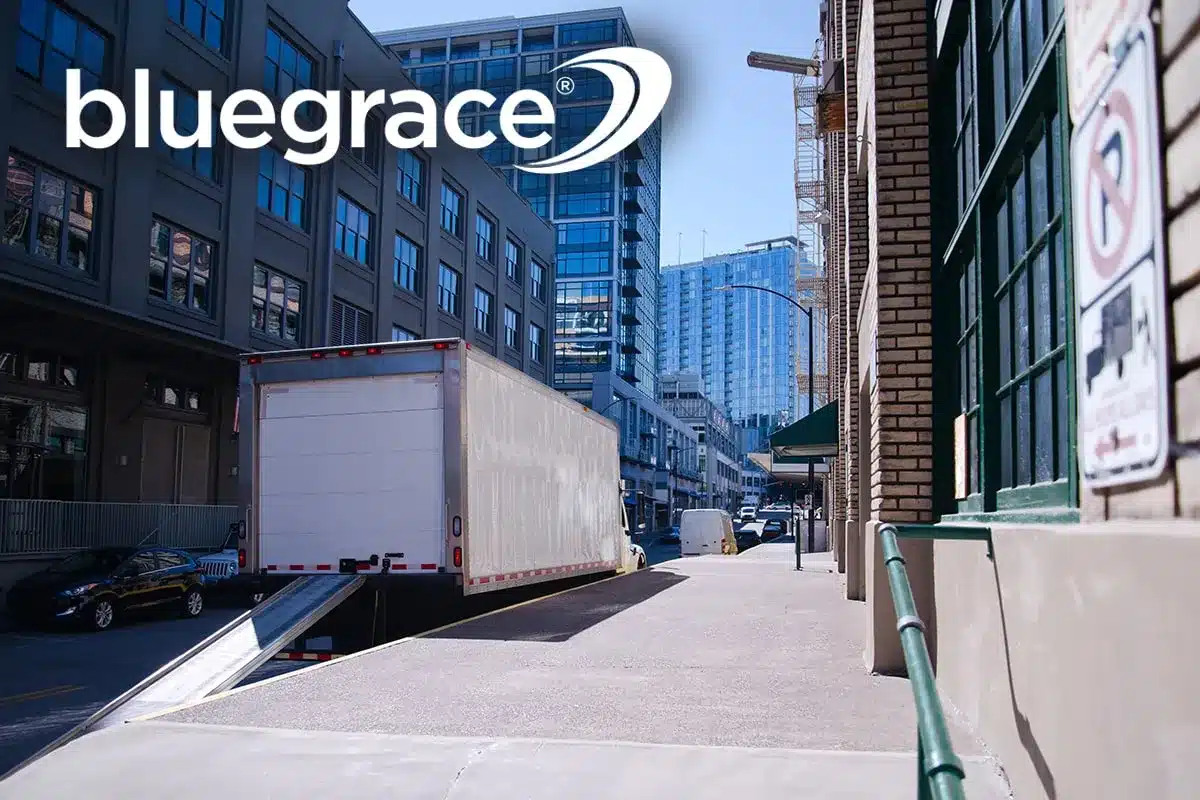 White delivery truck with loading ramp at an urban warehouse with BlueGrace logo.