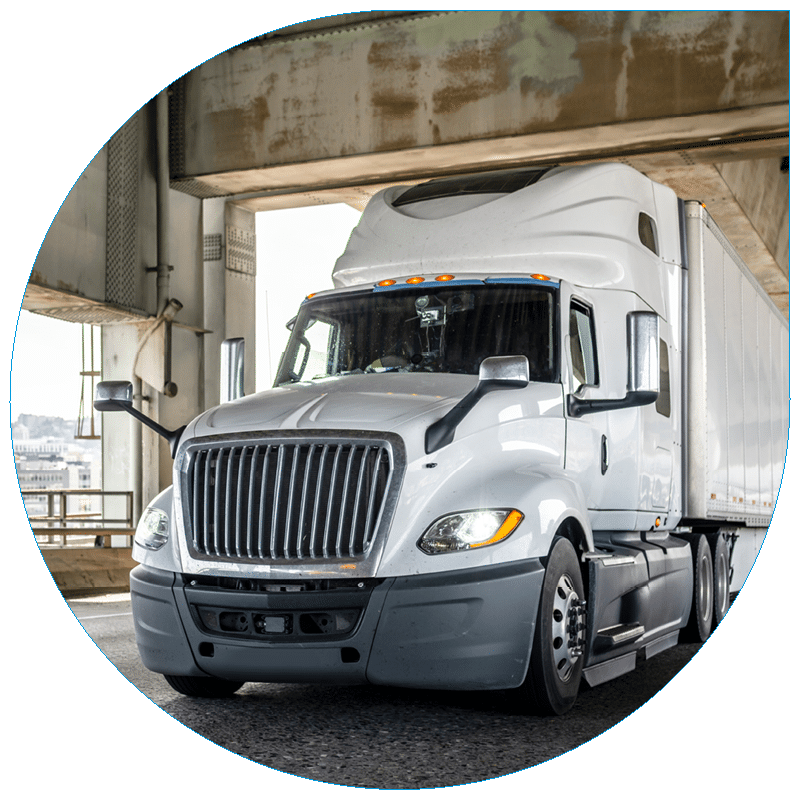 Low-angle view of a modern white semi-truck and trailer parked under a concrete highway overpass, representing heavy-duty commercial transportation.