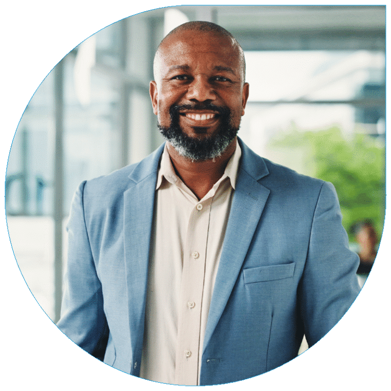 Portrait of a smiling professional man wearing a light blue suit jacket and beige button-down shirt in a bright office setting.