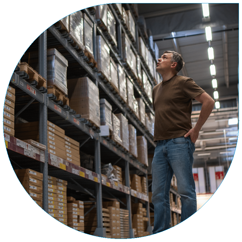 Low-angle view of a warehouse staff member looking up to inspect parcel inventory on high storage racks.
