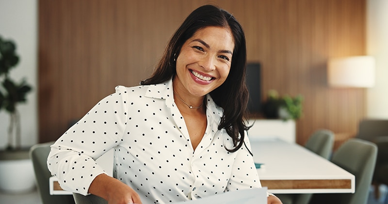 Smiling woman in a polka dot blouse sitting in a modern office or meeting room.