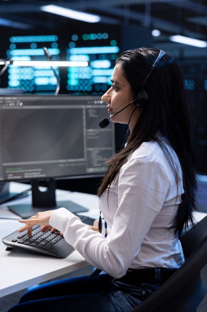 female agent talking to customer on headset while working on desktop computer