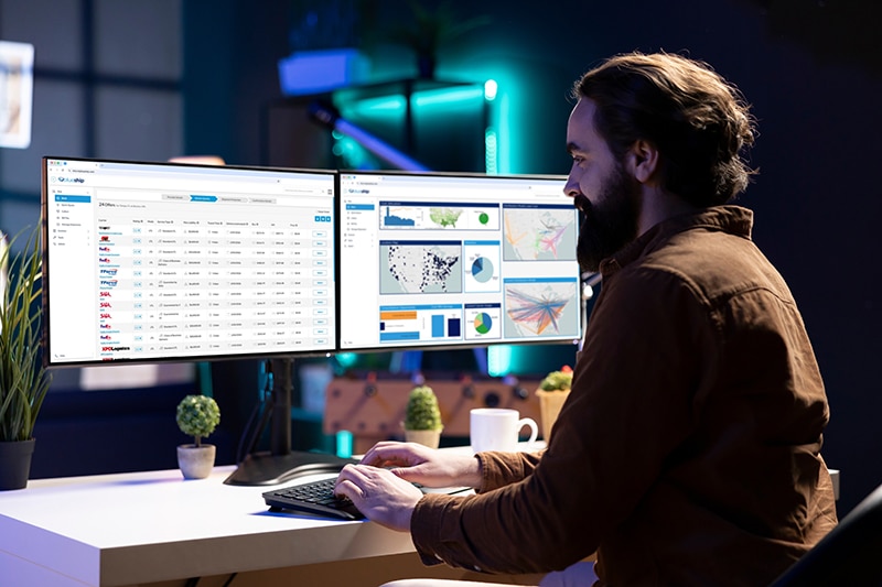 smiling logistics expert working on dual monitors