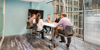 Small team of professionals collaborating at a high-top table in a modern office space with floor-to-ceiling windows overlooking the city.