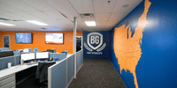 Office corridor featuring a large 'BG University' logo shield and an orange map of the United States on a blue wall, adjacent to employee cubicles.