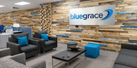 Modern corporate reception area featuring a rustic wood accent wall with the Bluegrace logo, accompanied by grey armchairs and blue decor accents.