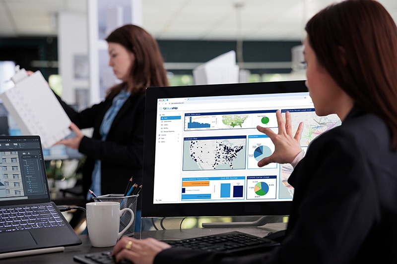 Woman in a blazer analyzing the BlueShip logistics dashboard on a monitor in a modern collaborative office