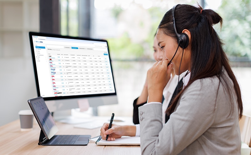 Asian Woman Wearing Headset Sitting At Desk Working In Office Call Centre Team