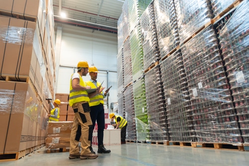 Manufacturing Logistics Solutions warehouse workers consult delivery plans using laptop and electronic database on tablet