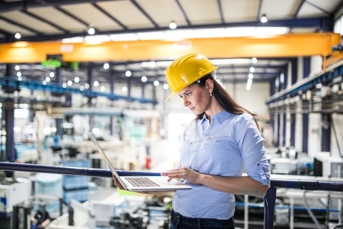 Manufacturing female manager reviewing data on laptop in manufacturing plant